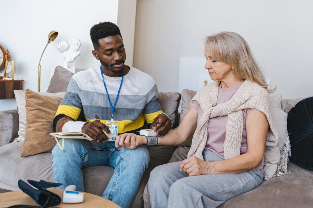 Volunteer checking elderly womans blood pressure at home. Compassionate healthcare support.